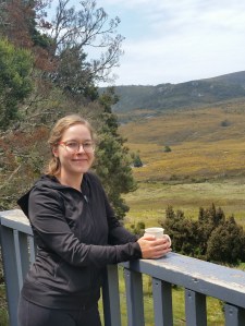 photo of Natalie Roth with a cup of tea on a porch, with rolling hills behind