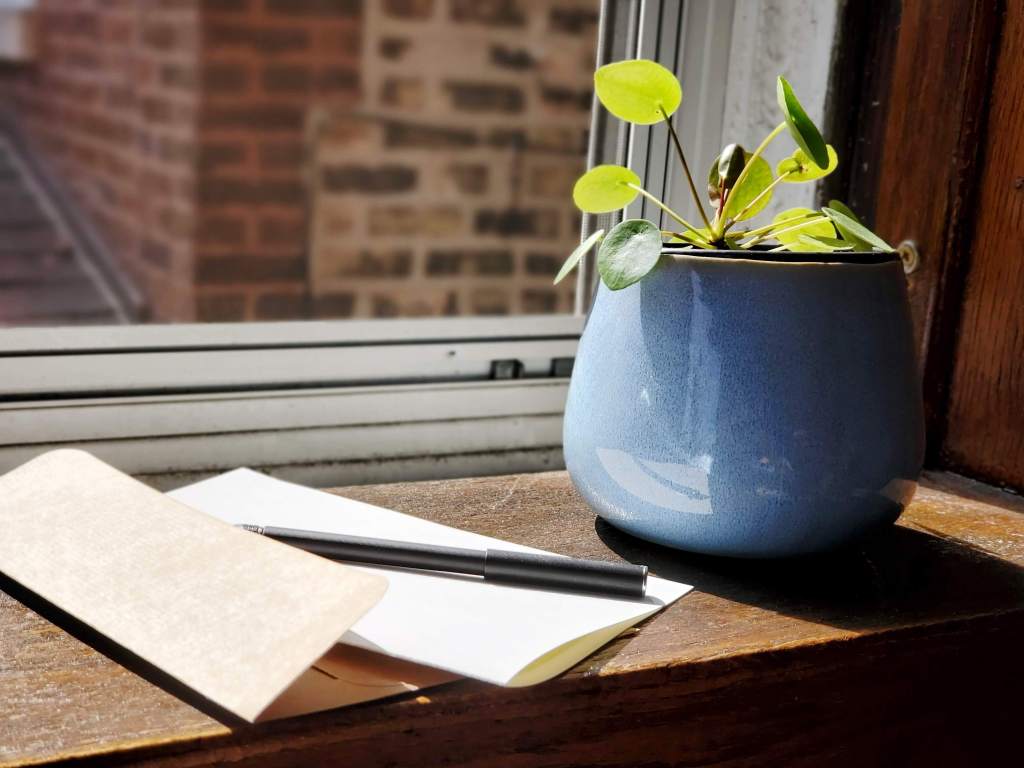 Photo of a blank card next to a sunny window sill, with a pen ready to write.
